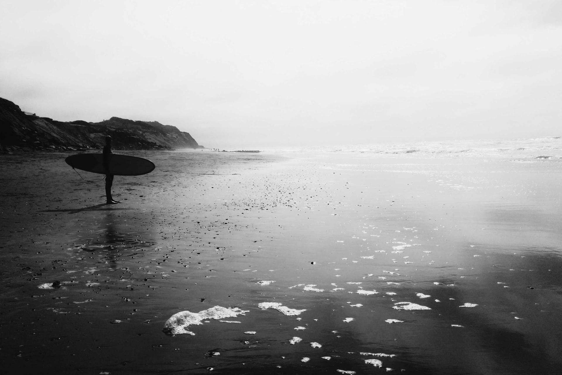 A lone figure standing still on a quiet, misty shoreline